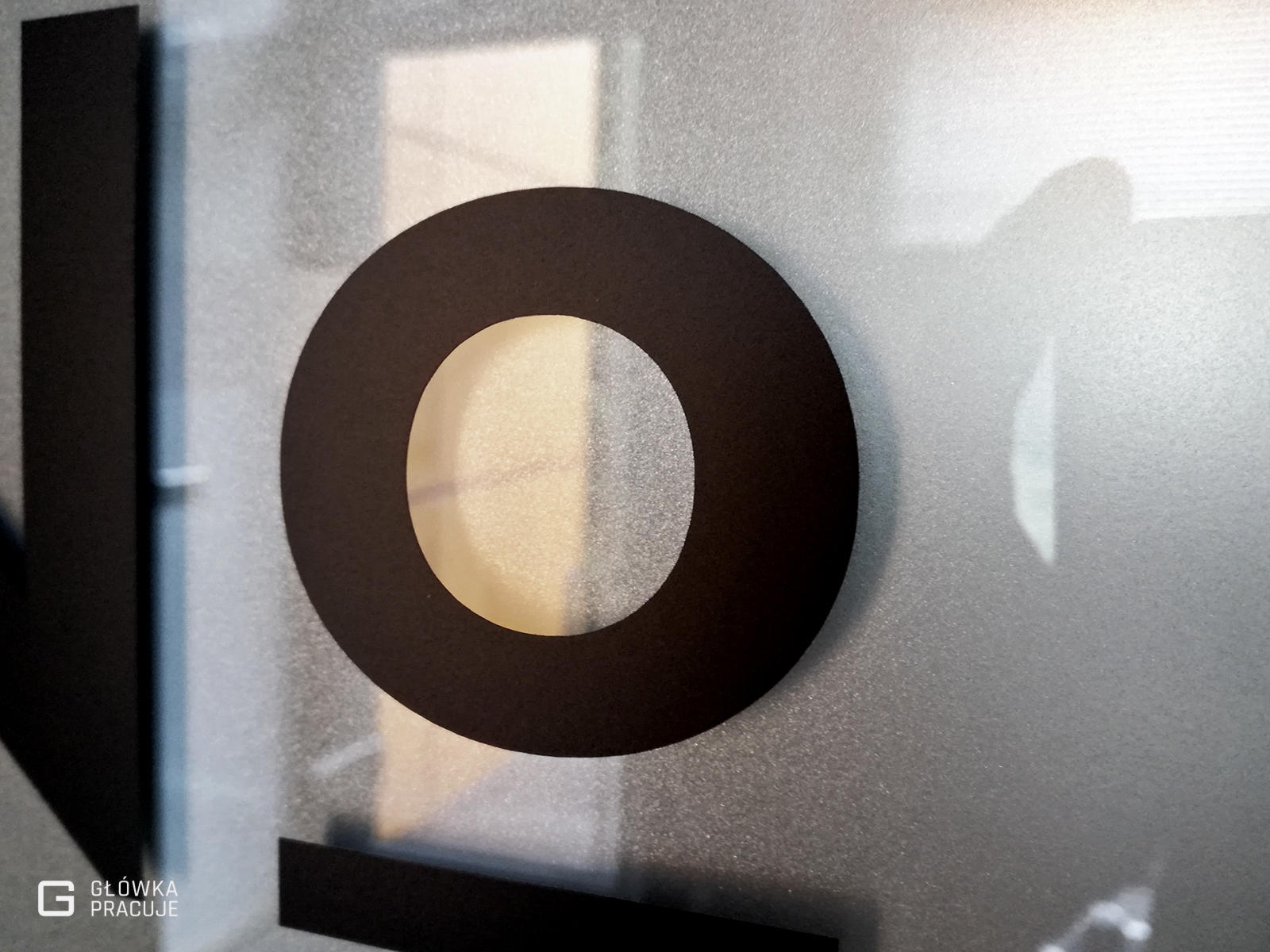 Główka Pracuje pl Number Coffee logotyp wycięty z czarnej folii naklejony na szklane drzwi z matową folią